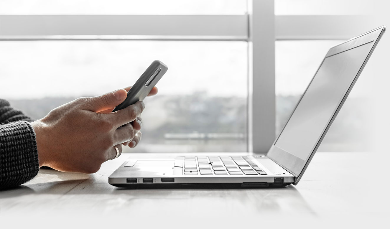Primer plano de una manos con un móvil delante de un PC. En MENTORAES ofrecemos coaching ejecutivo